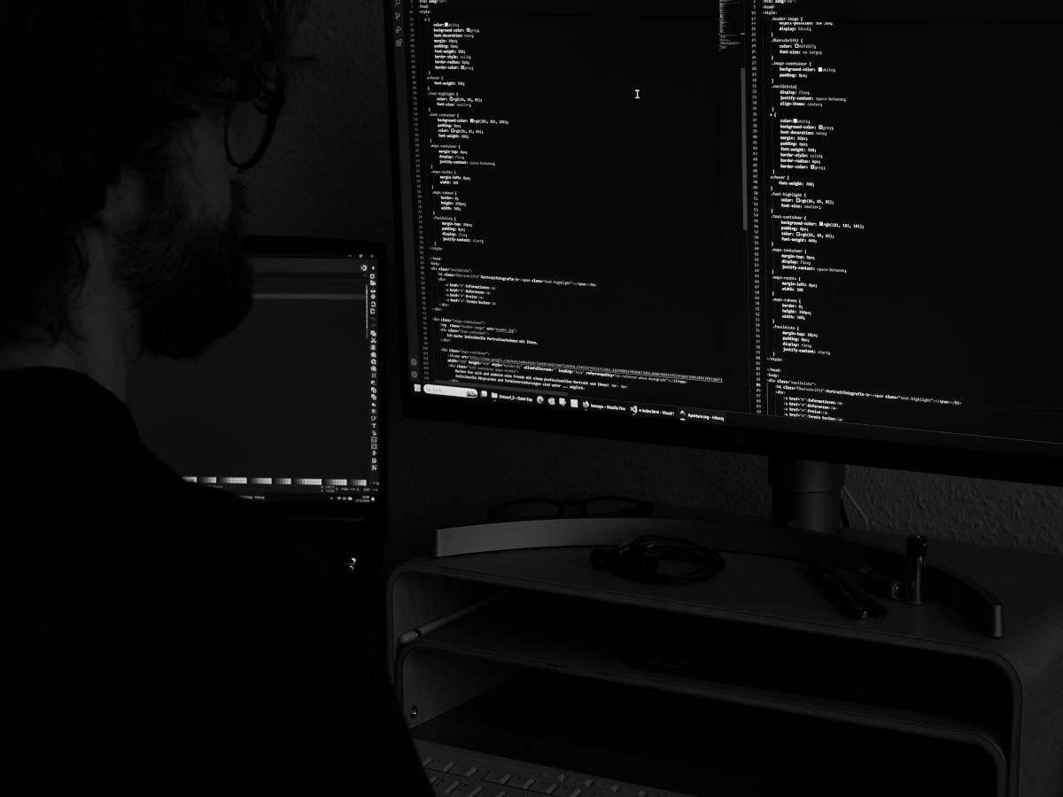 Bild von einem Mann über die Schulter fotografiert mit Blick auf einen Monitor auf dem Code zu sehen ist